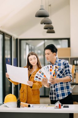 Birlikte çalışan mühendis ekipleri, mimari proje sahasında birlikte kask takıp model ev yapıyorlar. Modern ofiste Asya endüstrisi profesyonel takımı