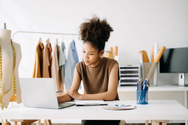Başarılı bir moda tasarımcısı. Atölyede dururken gülümseyen çekici genç bir kadın. Stüdyodaki masasında güzel bir iş kadını var..