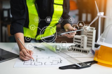 Yaratıcı mimarın orta bölümündeki inşaat simgeleri modern ofisteki masalarda mimari projeler üzerinde çalışıyor