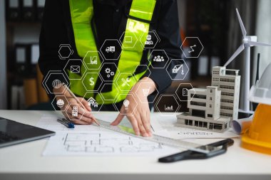 Yaratıcı mimarın orta bölümündeki inşaat simgeleri modern ofisteki masalarda mimari projeler üzerinde çalışıyor