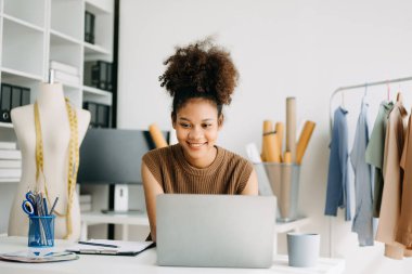 Başarılı bir moda tasarımcısı. Atölyede dururken gülümseyen çekici genç bir kadın. Stüdyodaki masasında güzel bir iş kadını var..