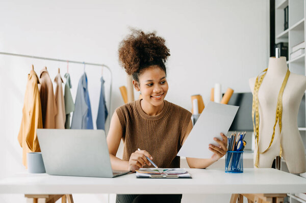 Успешный модельер. Привлекательная молодая женщина с улыбкой, стоя в мастерской. Владелица бизнеса за рабочим столом в студии.