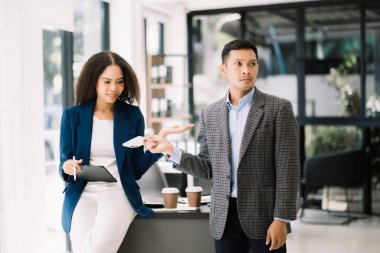 Nazik yönetici yönetici iş çözümlerini modern ofiste Asyalı kadın pazarlama yöneticisiyle paylaşır ve tartışır.