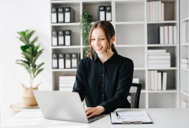 Kendine güvenen iş uzmanı çekici, gülümseyen genç bir kadın yaratıcı ofisin masasında dizüstü bilgisayarda çalışıyor.