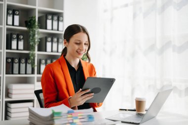 Kendine güvenen iş uzmanı çekici, gülümseyen genç bir kadın yaratıcı ofisteki masada tablet bilgisayarda çalışıyor.