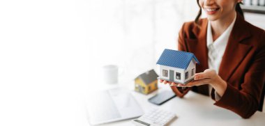 Kadın emlakçı, emlak ticareti, ofis masasından satın alma gibi konularda kırmızı çatıyı korumak için el kullanıyor.