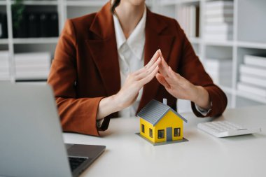 Kadın emlakçı, emlak ticareti, ofis masasından satın alma gibi konularda kırmızı çatıyı korumak için el kullanıyor.