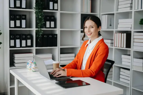 Confident business expert attractive smiling young woman working on laptop computer at desk in creative office