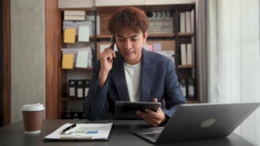 Genç iş adamı iş yerinde otururken dizüstü bilgisayar ve tablet kullanıyor. İşine odaklan..