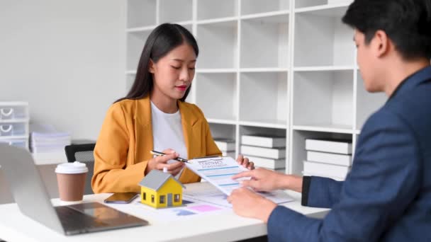 アジアの女性不動産エージェントは 契約に署名している男性に家を販売しています テーブルの上に小さなトイハウス 不動産保険のコンセプト — ストック動画