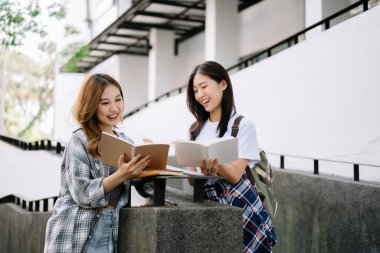 İki zeki Asyalı üniversite öğrencisi üniversitenin merdivenlerinde kitap okuyor. 