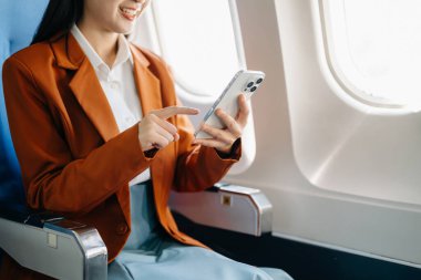 Çekici Asyalı kadın yolcu rahat koltukta oturmuş kablosuz bağlantıyı kullanarak akıllı telefon üzerinde çalışıyor. Stil içinde seyahat et, zarafetle çalış.