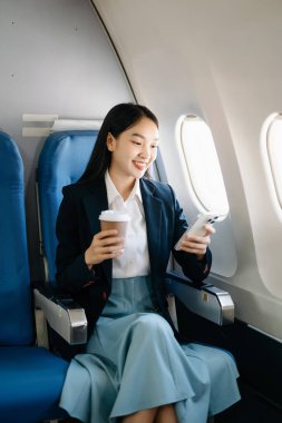 Çekici Asyalı kadın yolcu rahat koltukta oturmuş kablosuz bağlantıyı kullanarak akıllı telefon üzerinde çalışıyor. Stil içinde seyahat et, zarafetle çalış.