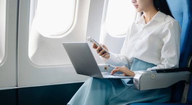 Çekici Asyalı kadın yolcu rahat koltukta oturmuş kablosuz bağlantı kullanarak dizüstü bilgisayarla kablosuz bağlantı kuruyor. Stil içinde seyahat et, zarafetle çalış.