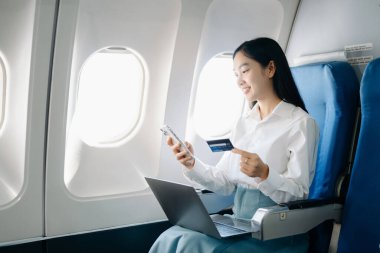 Çekici Asyalı kadın yolcu rahat koltukta oturmuş kablosuz bağlantı kullanarak dizüstü bilgisayarla kablosuz bağlantı kuruyor. Stil içinde seyahat et, zarafetle çalış.