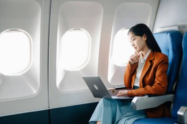Çekici Asyalı kadın yolcu rahat koltukta oturmuş kablosuz bağlantı kullanarak dizüstü bilgisayarla kablosuz bağlantı kuruyor. Stil içinde seyahat et, zarafetle çalış.