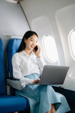 Çekici Asyalı kadın yolcu rahat koltukta oturmuş kablosuz bağlantı kullanarak dizüstü bilgisayarla kablosuz bağlantı kuruyor. Stil içinde seyahat et, zarafetle çalış.