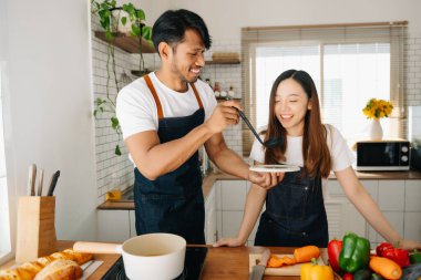 Sabah karısı ona sarılırken mutfakta ekmek ve meyveyle yemek hazırlayan bir adam.