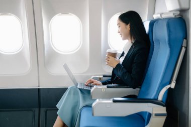 Çekici Asyalı kadın yolcu rahat koltukta oturmuş kablosuz bağlantı kullanarak dizüstü bilgisayarla kablosuz bağlantı kuruyor. Stil içinde seyahat et, zarafetle çalış.