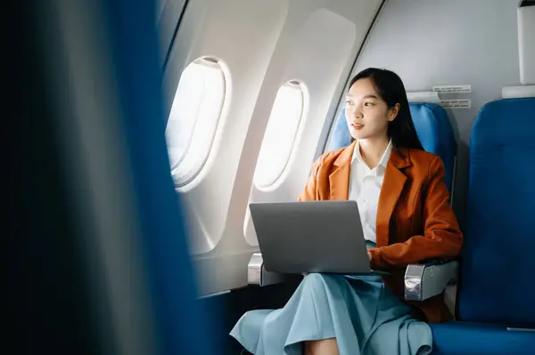 Attractive Asian female passenger of airplane sitting in comfortable seat while working on laptop computer with mock up area using wireless connection. Travel in style, work with grace