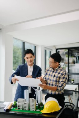 Two colleagues discussing data working with architectural project at construction site at desk in office
