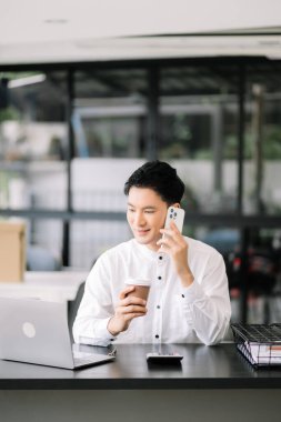 Tablet ve dizüstü bilgisayarda yazan yakışıklı genç adam ahşap masa modern ofisinde otururken.