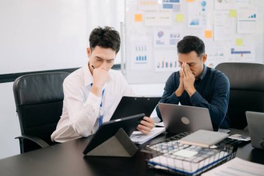 İki Asyalı iş adamı akıllı telefonla konuşuyor ve ofiste dizüstü bilgisayar kullanıyorlar.