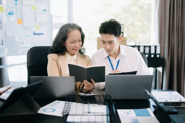 Nazik yönetici yönetici, Asyalı bayan pazarlama yöneticisiyle iş çözümlerini dizüstü bilgisayarda paylaşır ve tartışır..