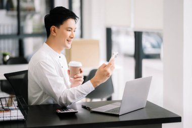 Tablet ve dizüstü bilgisayarda yazan yakışıklı genç adam ahşap masa modern ofisinde otururken.