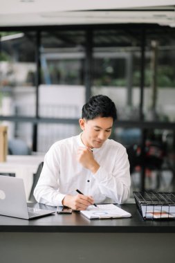 Tablet ve dizüstü bilgisayarda yazan yakışıklı genç adam ahşap masa modern ofisinde otururken.