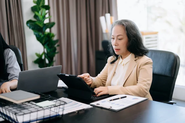 Mature businesswoman executive manager looking at laptop watching online webinar training or having virtual meeting video conference doing market research working in office.