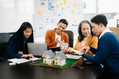 Mülk sektörünü dengelemek. Emlakçı ev tasarımını ve satın alma anlaşmasını görmek için ev tarzını anlatıyor. Modern ofiste ahşap bir ev.