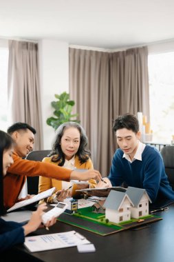 Mülk sektörünü dengelemek. Emlakçı ev tasarımını ve satın alma anlaşmasını görmek için ev tarzını anlatıyor. Modern ofiste ahşap bir ev.