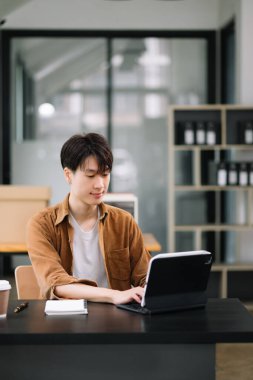 Kendine güveni olan Asyalı bir adam modern ofiste tablet bilgisayarda çalışıyor. 