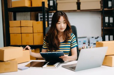 Genç işyeri sahibi kadın paket kutusu hazırlıyor ve online alışveriş konsepti üzerinde müşteriye teslim edilmesi için online olarak kontrol ediliyor.