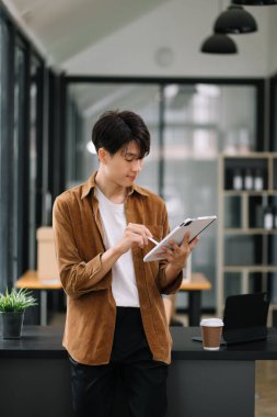 Modern ofiste elinde tablet bilgisayarla gülümseyen kendine güvenen Asyalı adam. 