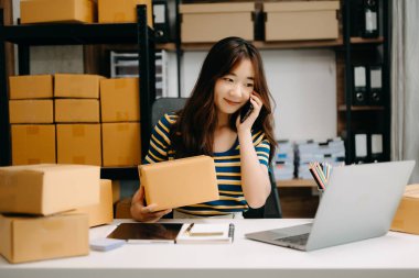 Genç işyeri sahibi kadın paket kutusu hazırlıyor ve online alışveriş konsepti üzerinde müşteriye teslim edilmesi için online olarak kontrol ediliyor.