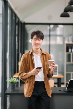 Genç adam iş yerinde akıllı telefon kullanıyor. Ofisteki işine odaklan.