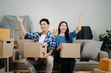 Büyük kutuları olan genç bir çift yeni bir eve taşınıyor, çift için yeni bir daire, genç Asyalı erkek ve kadın yeni ev için kanepenin taşınmasına yardım ediyorlar.