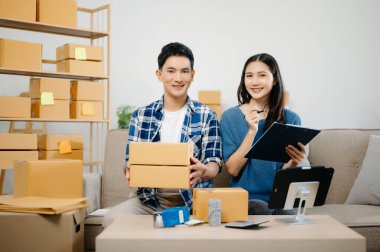 Başlangıçta küçük işletme KOBİ 'si, girişimci erkek ve kadın tablet kullanan girişimci, evdeki kanepede paket ürün kutusu hazırlamak için çevrimiçi alışveriş siparişini alır ve kontrol eder
