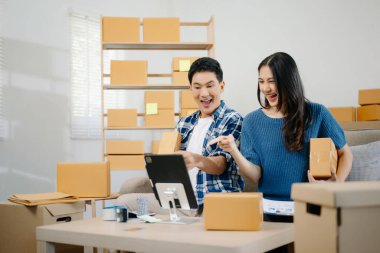 İki Asyalı blogcu, dükkanında canlı yayın yapmak için kameranın önünde kıyafetlerini gösteriyor. Çevrimiçi alışveriş arabası fikri. Evdeki kanepede.