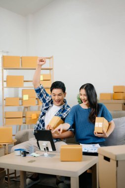 İki Asyalı blogcu, dükkanında canlı yayın yapmak için kameranın önünde kıyafetlerini gösteriyor. Çevrimiçi alışveriş arabası fikri. Evdeki kanepede.