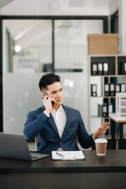 Asyalı işadamı ofisteki masada akıllı telefondan konuşuyor. 