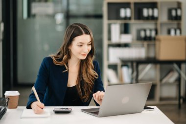 Modern ofiste dizüstü bilgisayar kullanan kendine güvenen bir kadın..