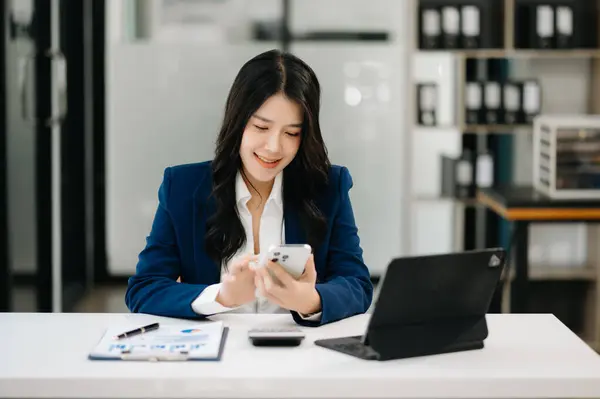 Confident business expert attractive smiling young woman typing on smartphone on desk in creative office