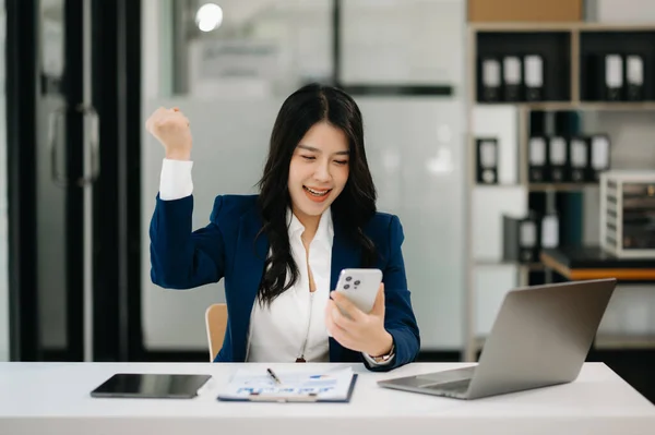 Confident business expert attractive smiling young woman holding smartphone at desk in creative office