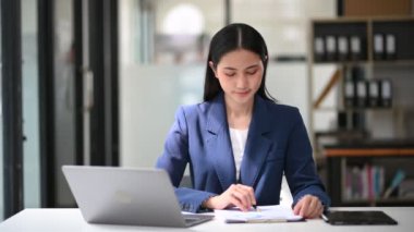 Dizüstü bilgisayarla çalışan Asyalı iş kadını ve ofiste belgeler 