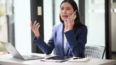 Ofiste çalışan Asyalı iş kadını akıllı telefonla konuşuyor ve dizüstü bilgisayar kullanıyor. 