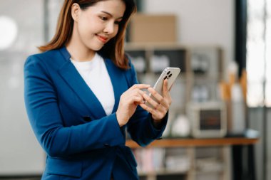 Modern ofiste akıllı telefon kullanan kendine güvenen Asyalı kadın.