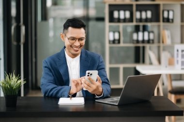 Genç ve çekici Asyalı iş adamı gülümseyip ofiste kameraya bakıyor.     